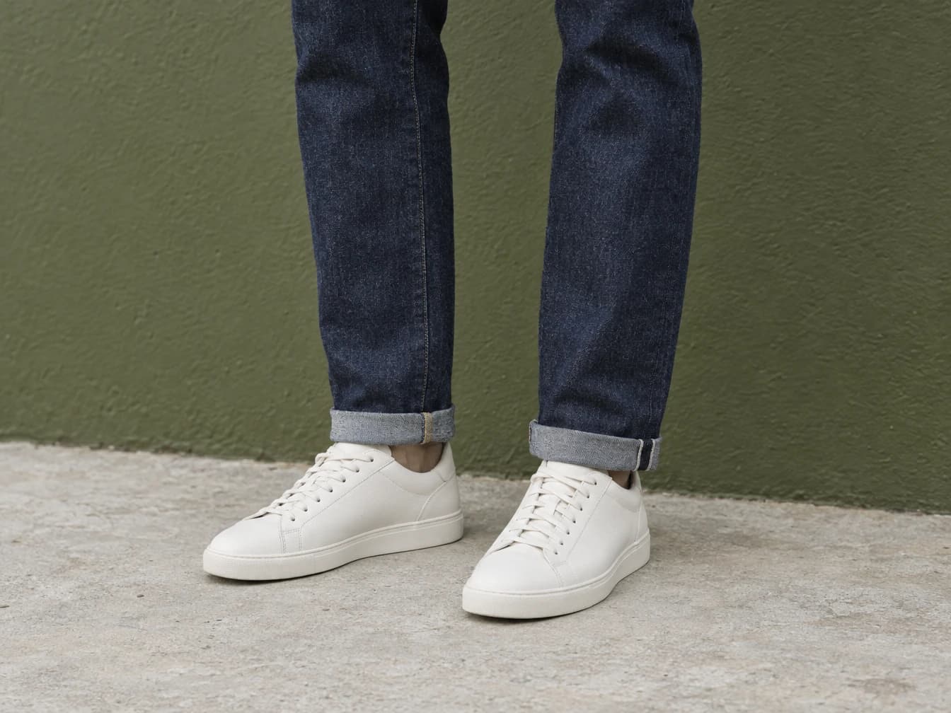 Dark indigo jeans with modest turn-ups above off-white low-top sneakers, showing a casual hem treatment.