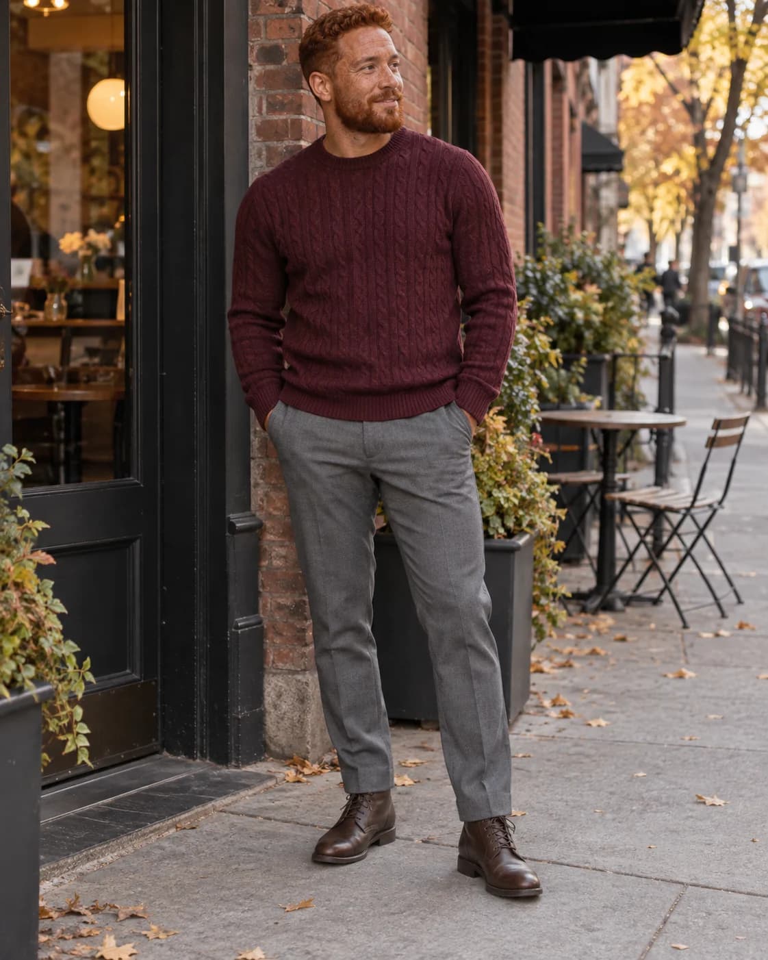 Red-haired man wearing a burgundy sweater, gray trousers and brown ankle boots
