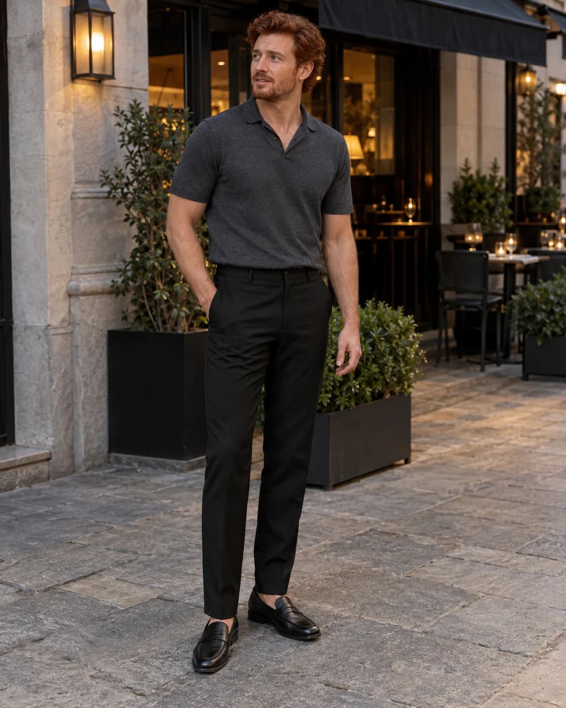 Auburn-haired man wearing a charcoal knit polo, black trousers and black penny loafers