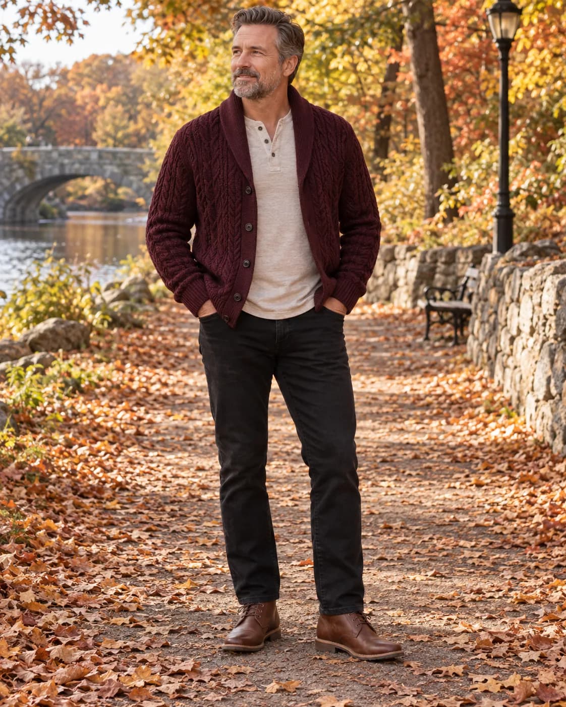 White man in a burgundy shawl-collar cardigan over an oatmeal Henley with black jeans and cognac chukkas on an autumn walk