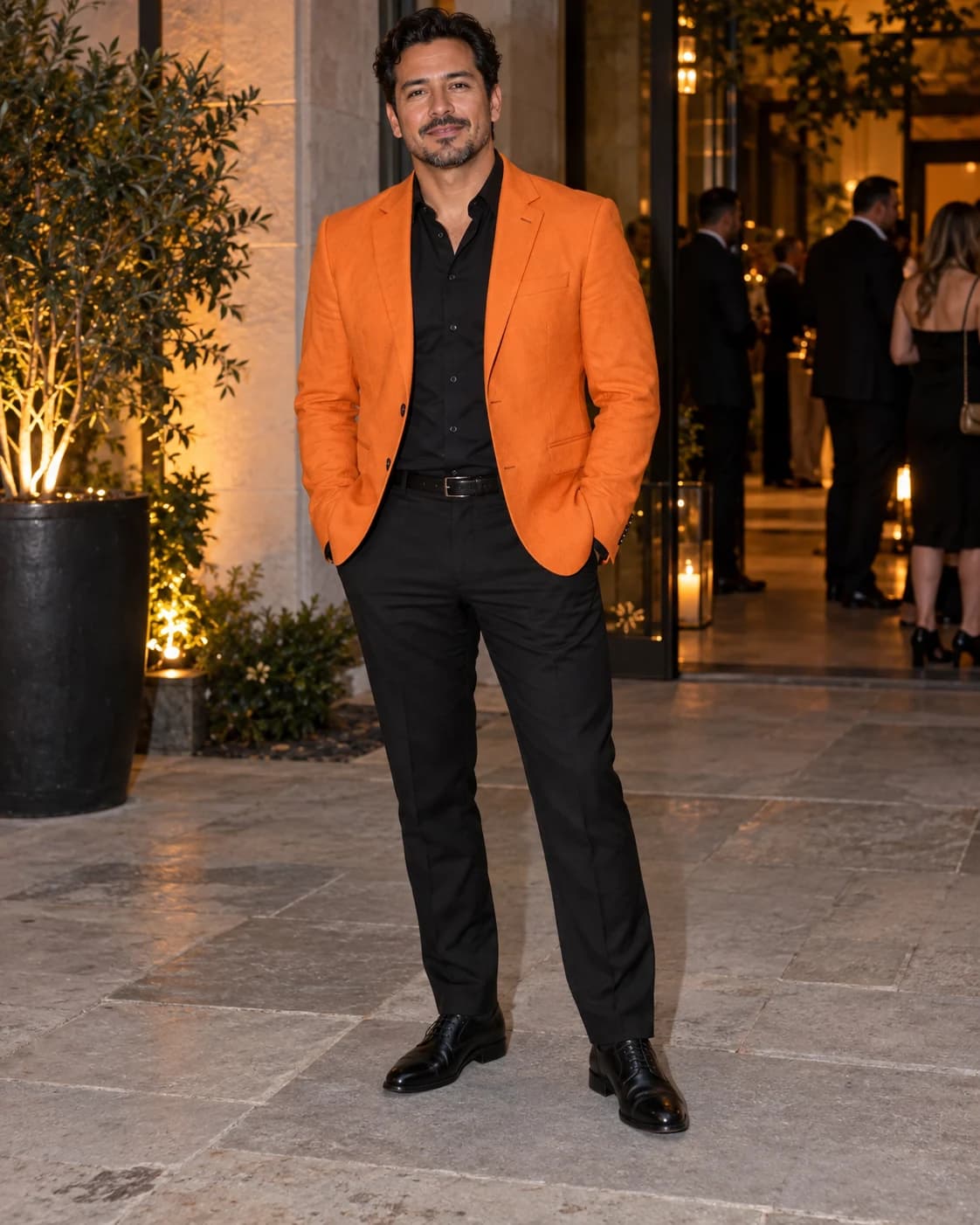 Adult Latino man wearing a solid orange sport coat over a black shirt with black trousers and black cap-toe shoes