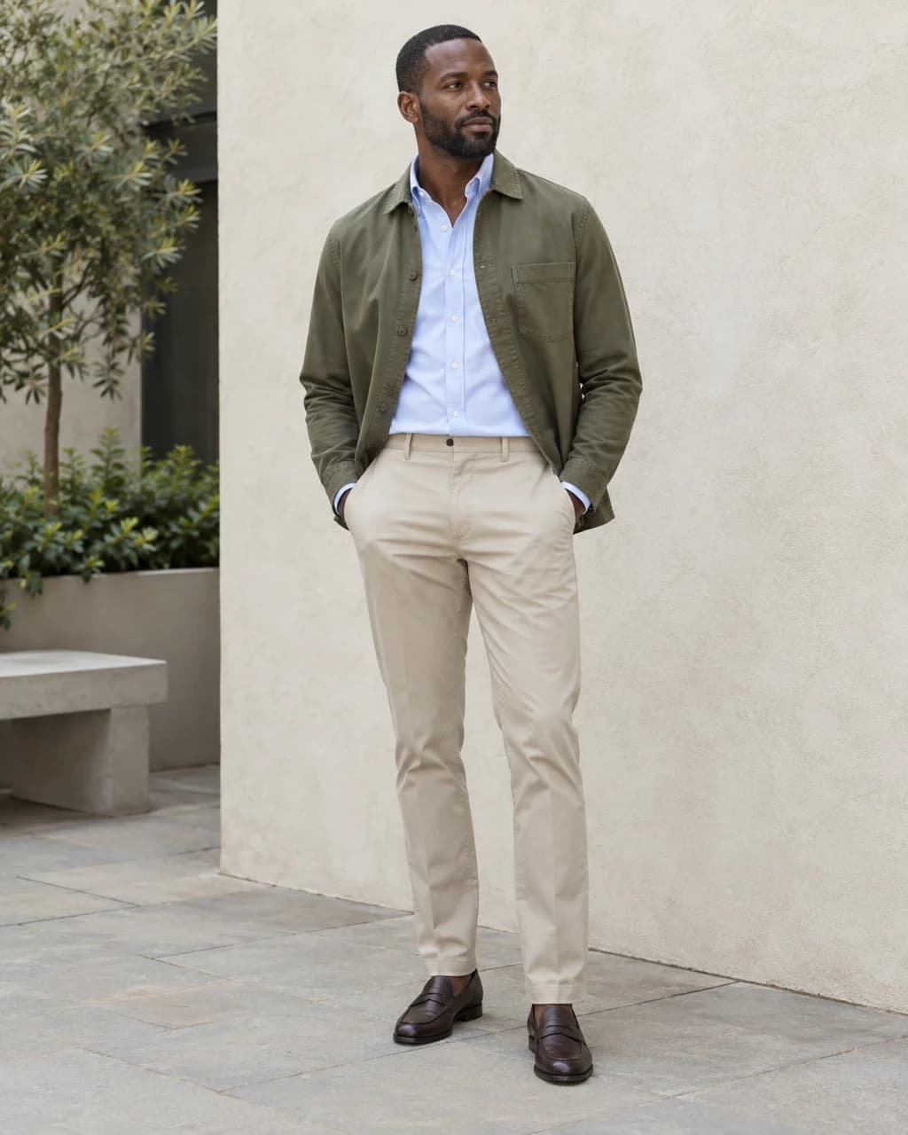 Man wearing an olive overshirt over a tucked blue Oxford, stone chinos and brown penny loafers