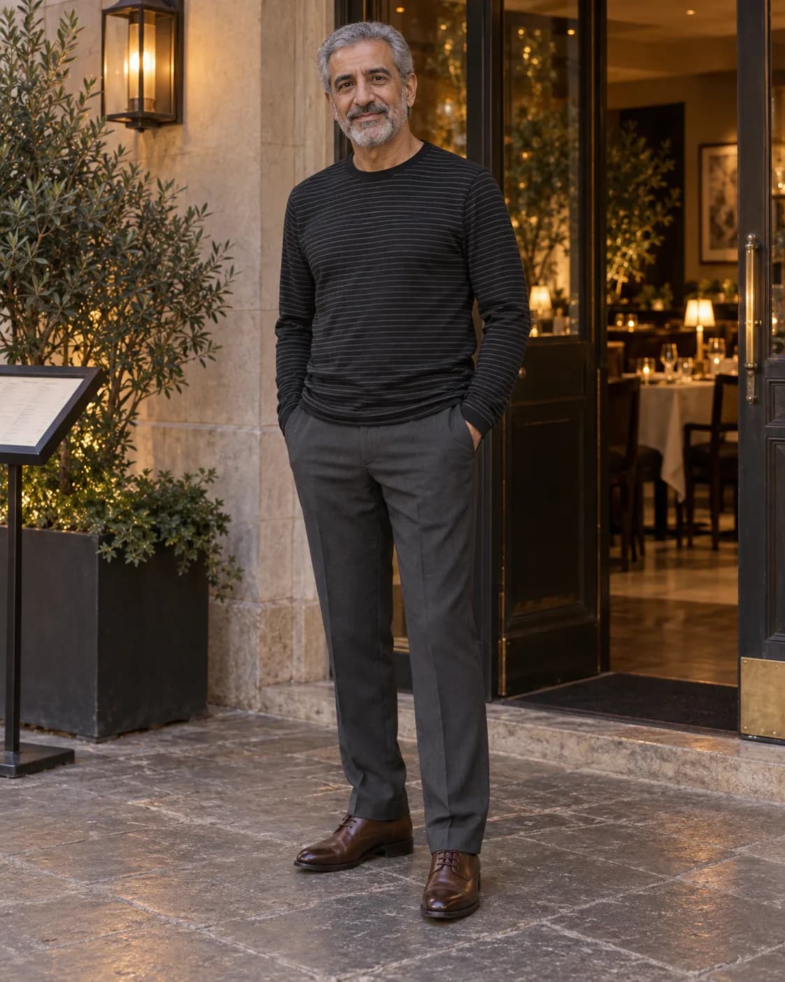 Middle Eastern man in a black-and-charcoal striped long-sleeve shirt with charcoal trousers and brown dress oxfords
