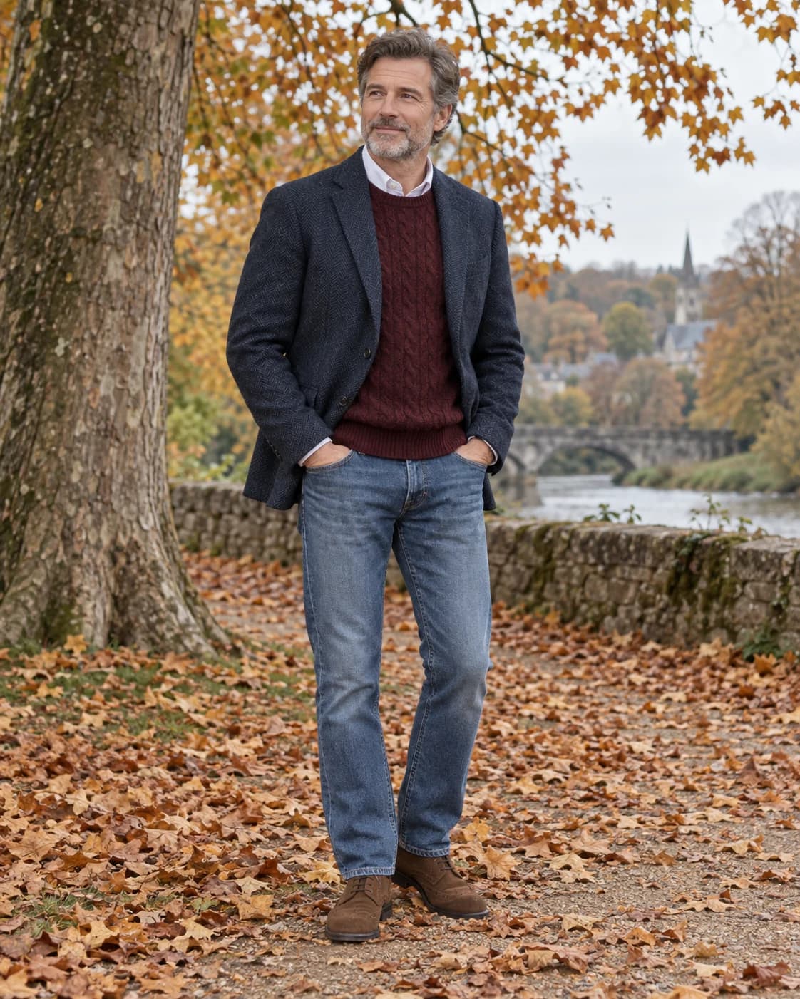 Adult white man in a navy herringbone blazer over a burgundy knit and white shirt with medium-wash jeans and suede shoes